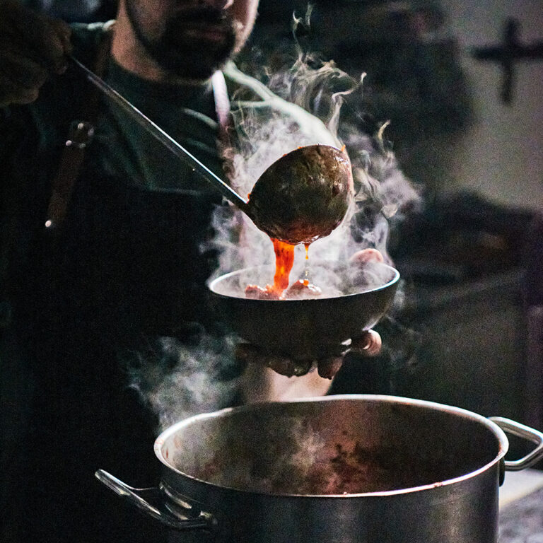 Person spooning sauce over a bowl of meatballs
