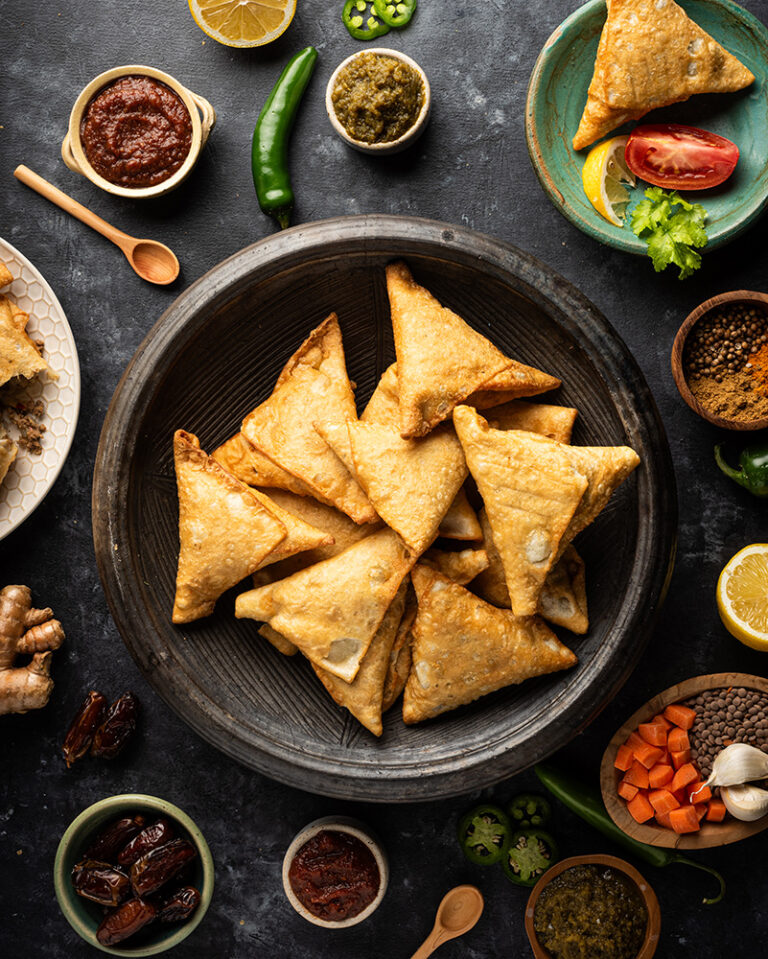 Sambusas in a black bowl surrounded by ingredients on a black tabletop