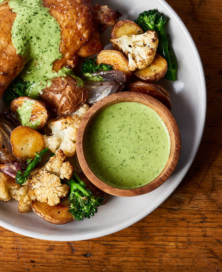 Small bowl of green sauce next to a bowl of roasted chicken and various veggies