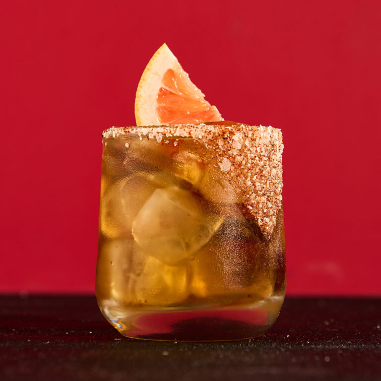 Margarita with salt and a grapefruit slice garnish on a red background