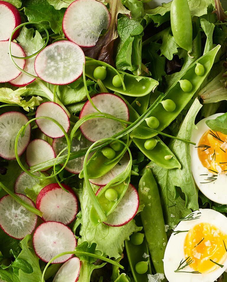 Sliced radishes, snap peas, and hard boiled eggs mixed salad greens