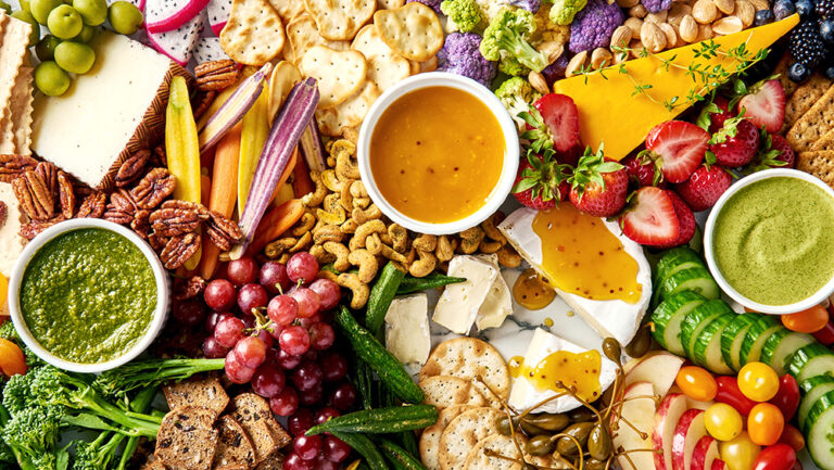 Overhead shot of a grazing board with fruit, veggies, cheese, crackers, nuts, and 3 chutney flavors