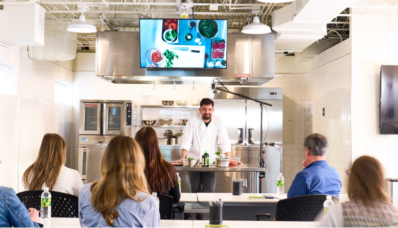 People in a kitchen watching a chef do a cooking demo