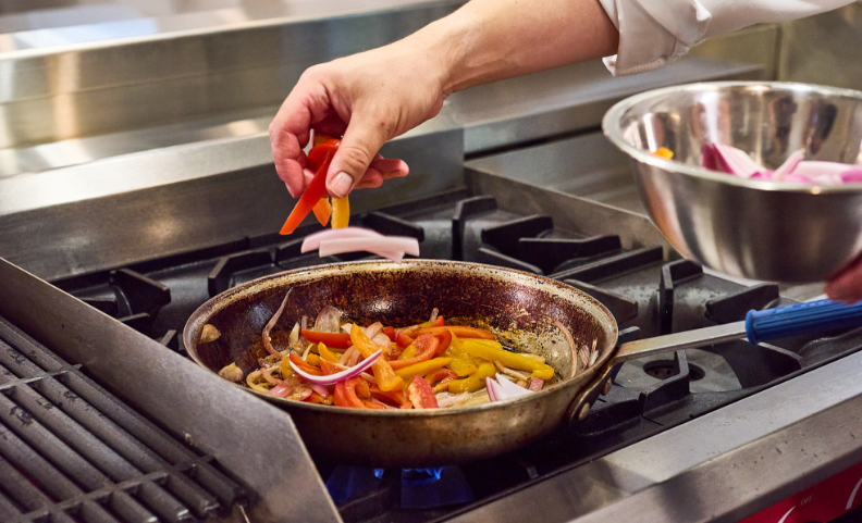 Person sprinkling sliced bell peppers into a pan over a stove